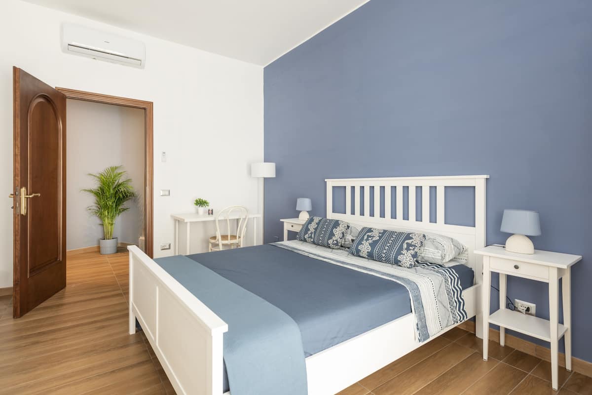 A bedroom with a bed, bedside tables, a lamp, a potted plant, and a door.