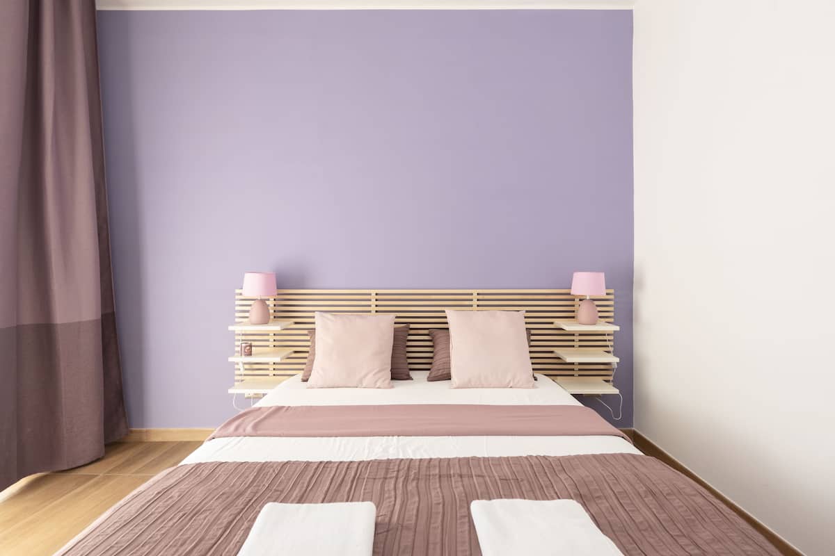 A neatly made bed with a wooden headboard, a bedside table with a lamp, and a curtain on the left.