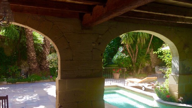 Zona de piscina al aire libre con arcos de piedra, una tumbona y una mesita.