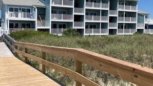 A beachfront hotel with multiple balconies and a wooden boardwalk leading to the entrance.