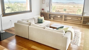 A modern living room with a large window offering a view of a desert landscape and mountains. - Casa Estela, quiet house with beautiful views (Villaverde, La Oliva)