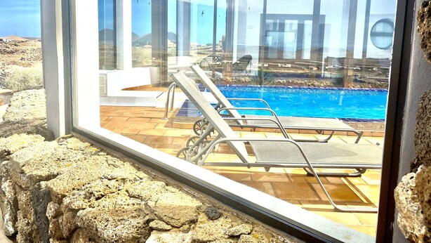 A modern pool area with clear glass walls, a pool, and lounge chairs. - Casa Estela, quiet house with beautiful views (Villaverde, La Oliva)