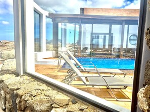 Un espace piscine moderne avec des parois en verre transparent, une piscine et des chaises longues.