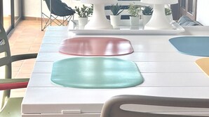 A dining table with colorful placemats, a chair, and a view of the outdoors through large windows. - Casa Estela, quiet house with beautiful views (Villaverde, La Oliva)