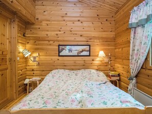 Habitación de cabaña de madera con una cama, dos lámparas de noche, un cuadro enmarcado en la pared y una ventana con cortinas.