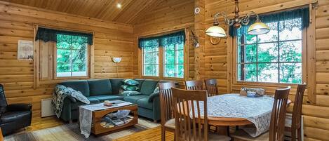 A cozy cabin interior with a wooden dining table, chairs, a sofa, and a coffee table.