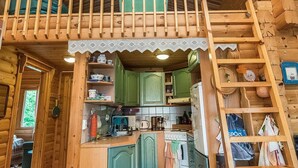 Une cabane en bois avec une chambre à coucher située en mezzanine, une cuisine avec des meubles verts et un petit coin repas.