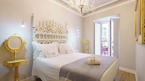 A bedroom with a large bed, a gold-framed mirror, a chandelier, and a white headboard. - Portuguese Soul Alfama | Terrace & River View | Sleeps 6 (Lisboa)