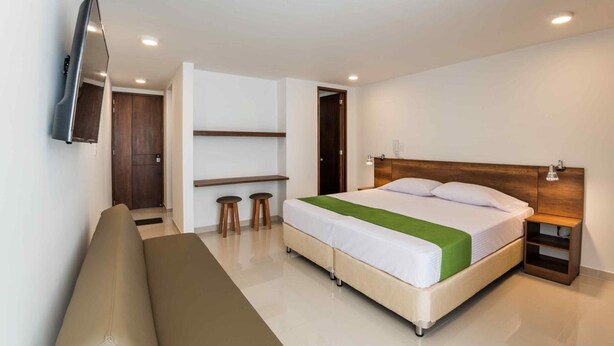 A modern hotel room with a bed, a sofa, a TV mounted on the wall, and a wooden headboard. - Altoprado Popayán (Popayán)