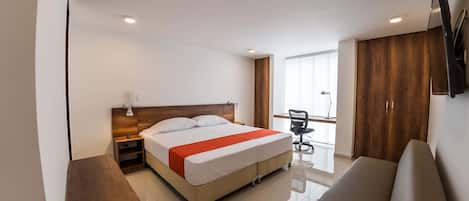 Una habitación de hotel moderna con cama, escritorio, silla, sofá y televisor en la pared.