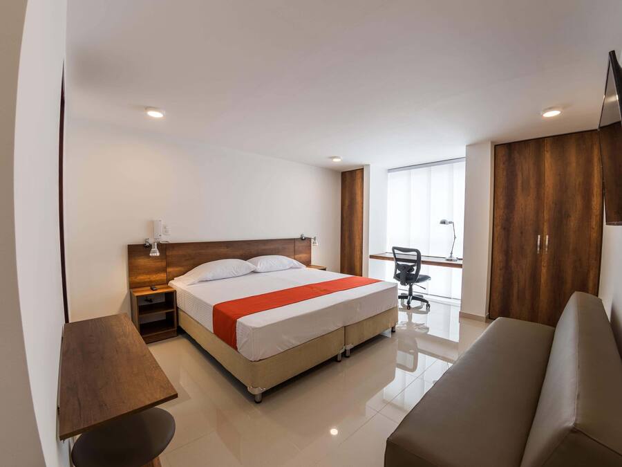Una habitación de hotel moderna con cama, escritorio, silla, sofá y televisor en la pared.