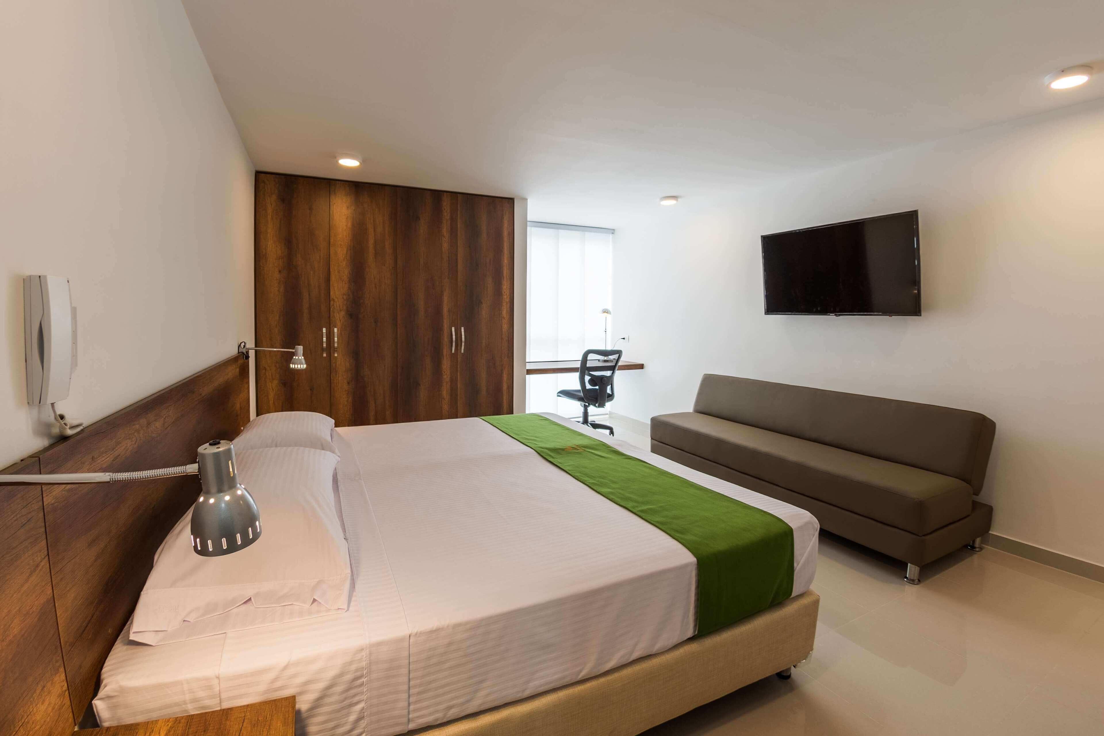 Een moderne hotelkamer met een groot bed, een slaapbank, een aan de muur bevestigde televisie en een bureau met een stoel.
