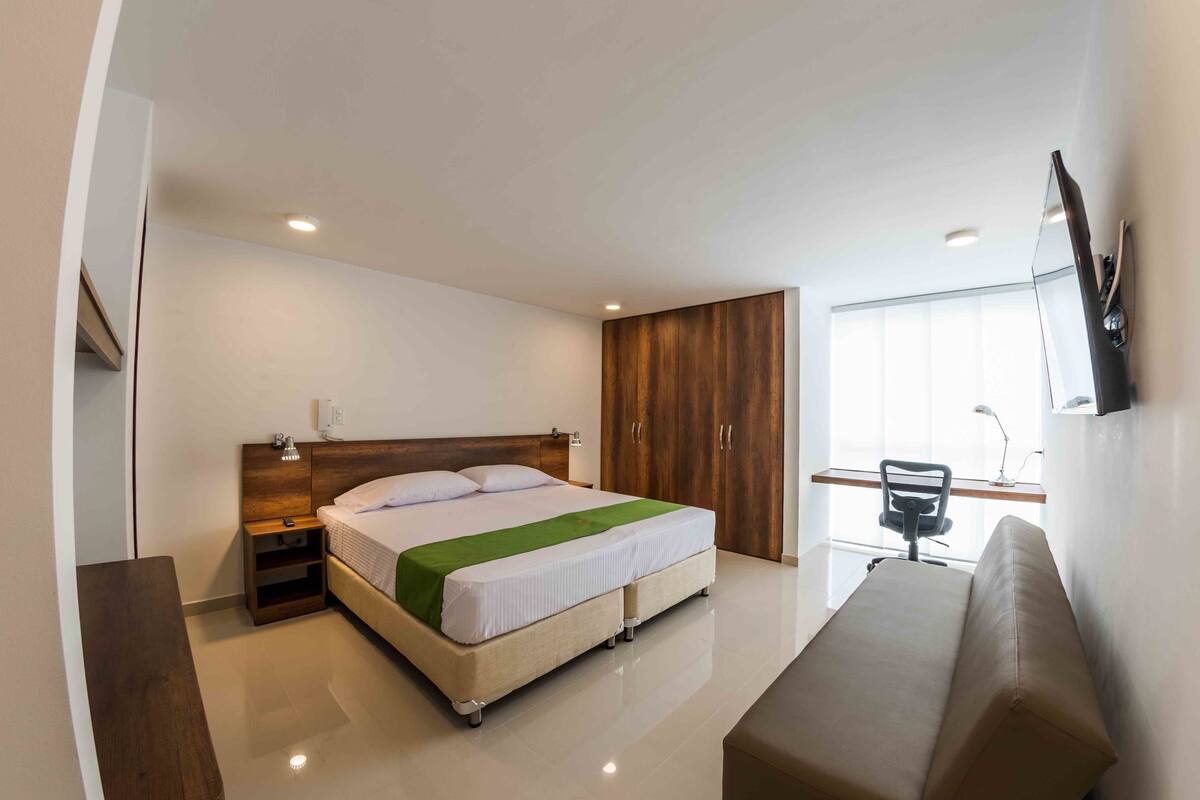 A modern hotel room with a large bed, bedside tables, a desk, and a chair.