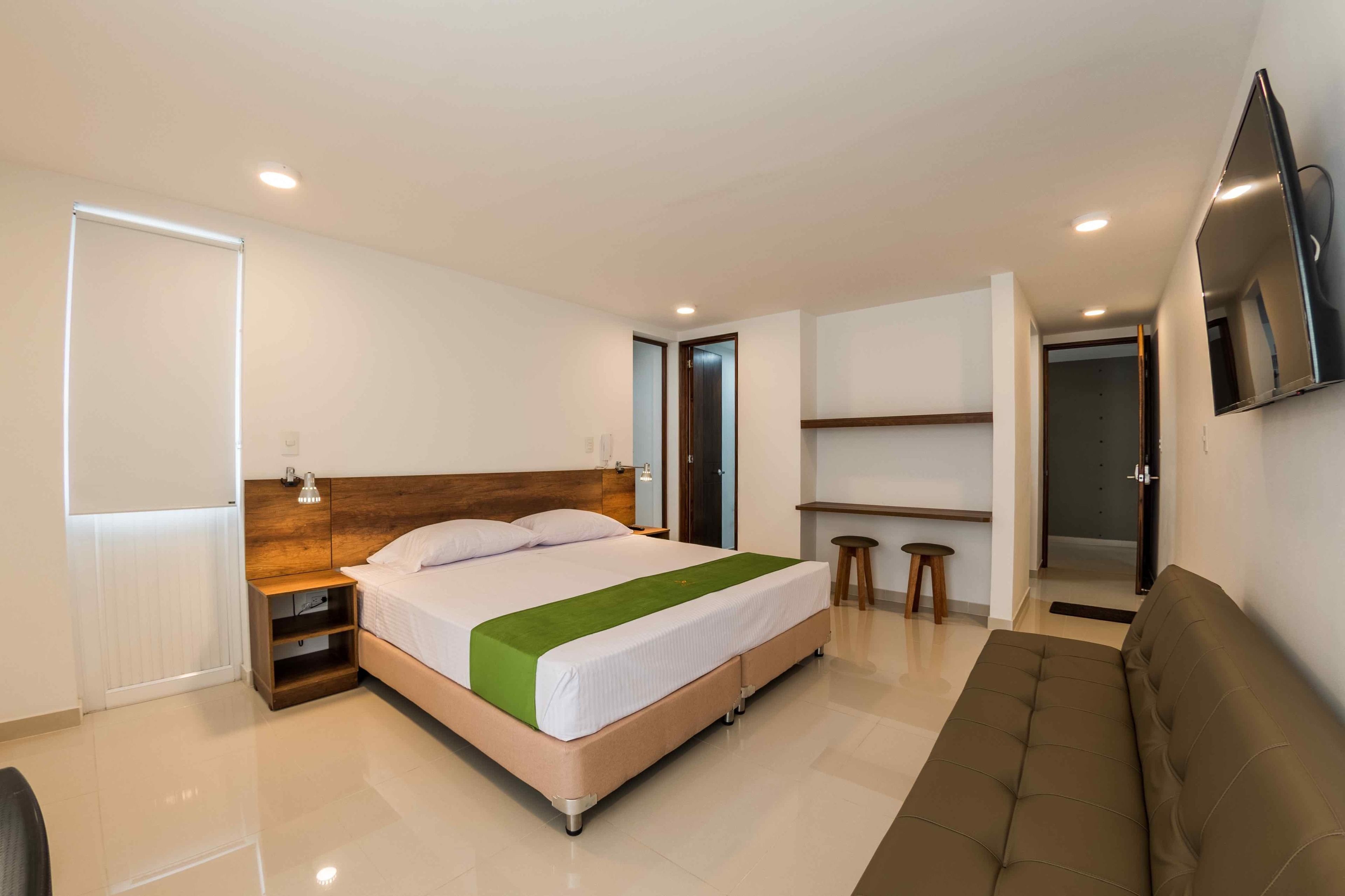 A modern hotel room with a large bed, a sofa, a TV, and a desk.