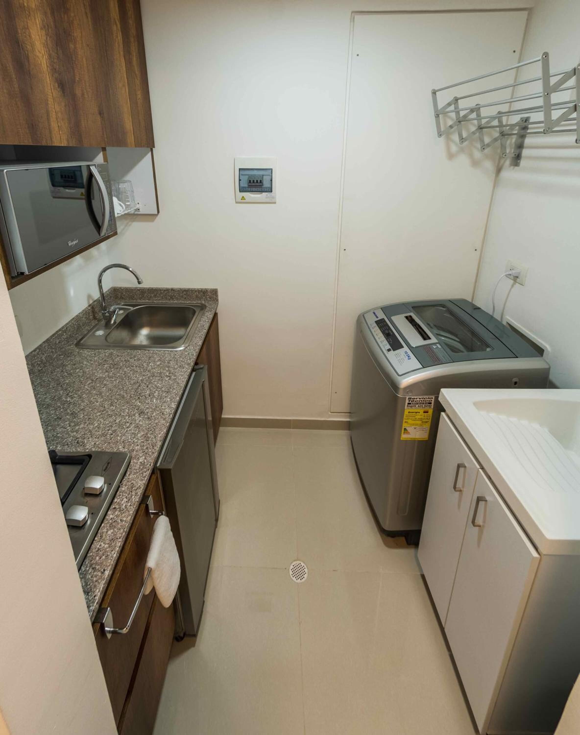 A compact kitchen with a microwave, sink, toaster, and a washing machine.