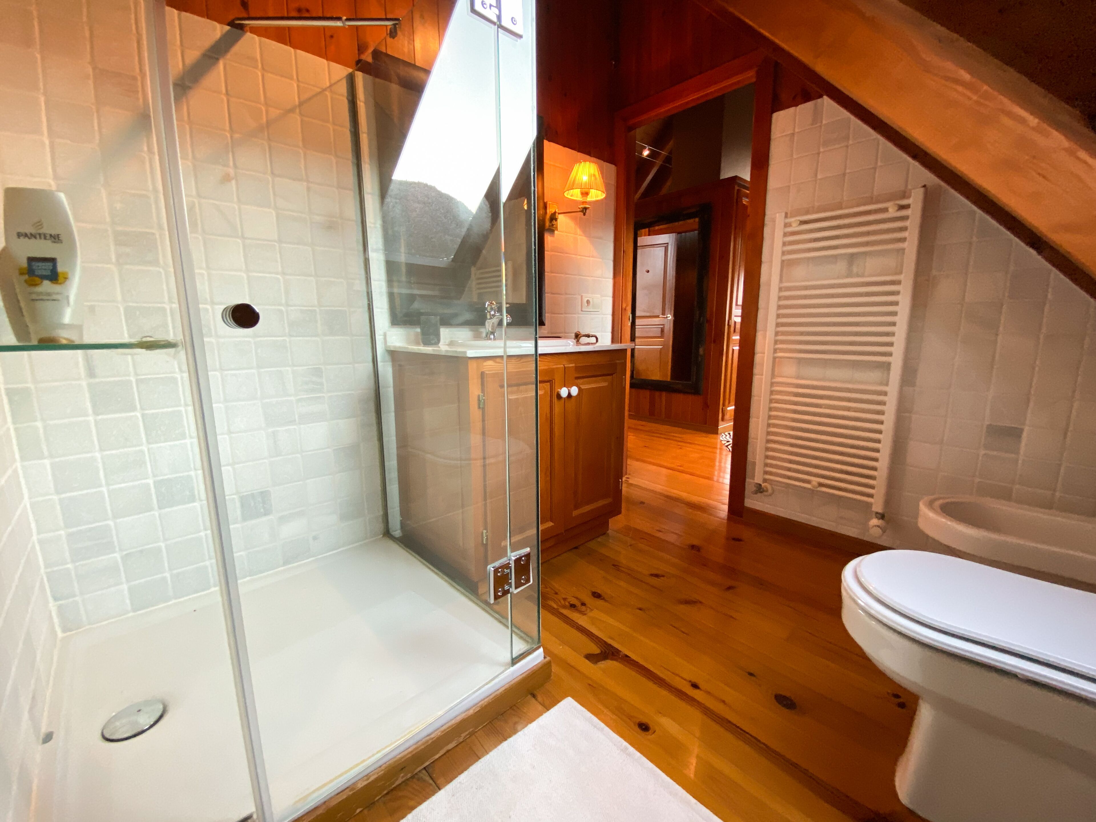 Un baño con cabina de ducha de vidrio, inodoro y suelo de madera.