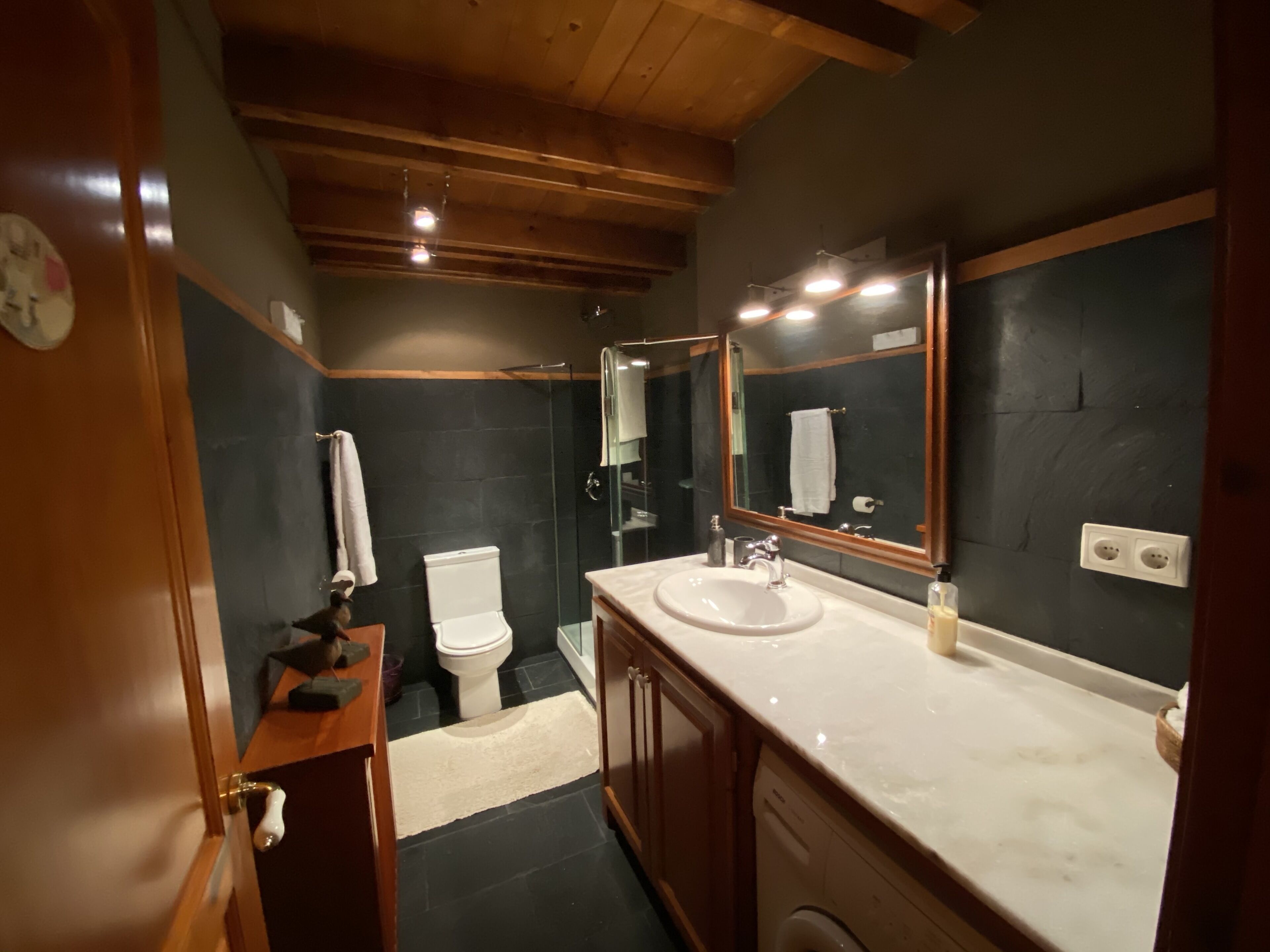 A bathroom with a wooden vanity, a sink, a mirror, a toilet, and a shower.