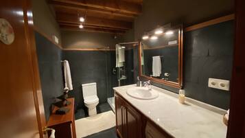 Un baño con tocador de madera, lavamanos, espejo, inodoro y ducha.