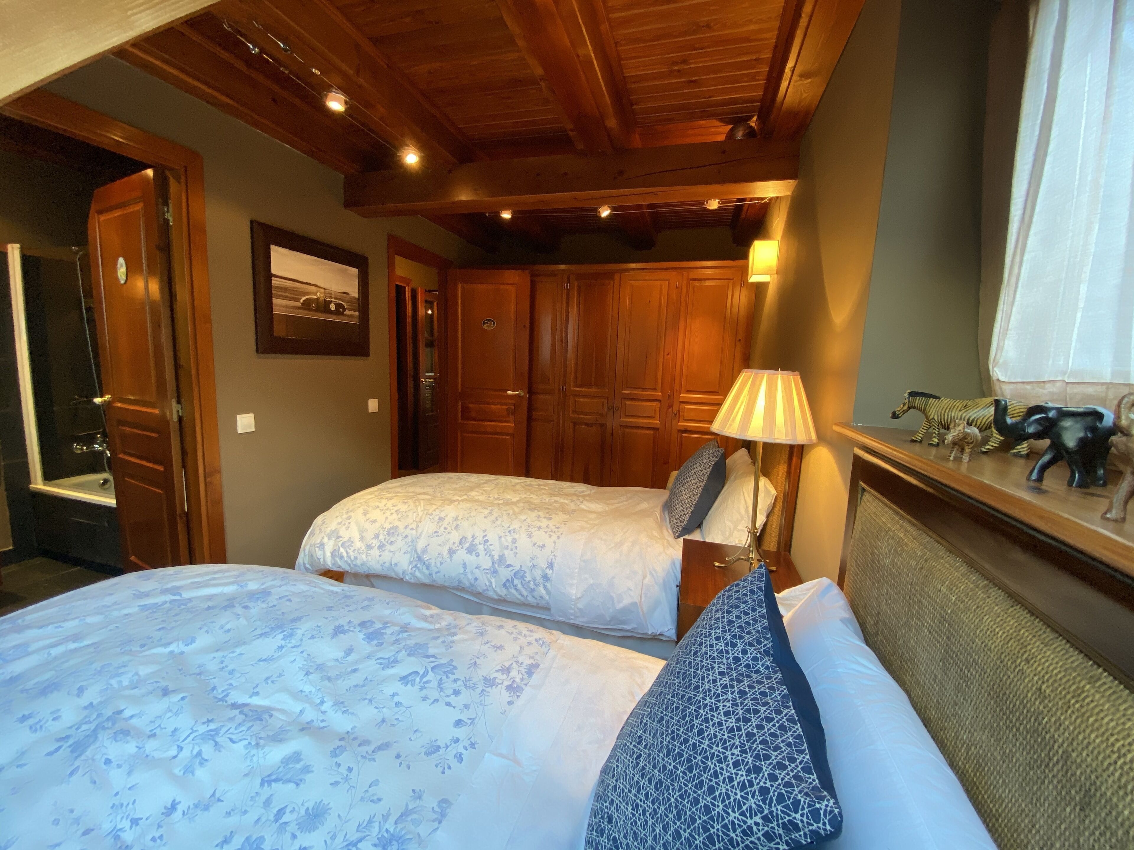 Un dormitorio con dos camas, un armario de madera, una mesita de noche, una lámpara y una ventana con cortinas.