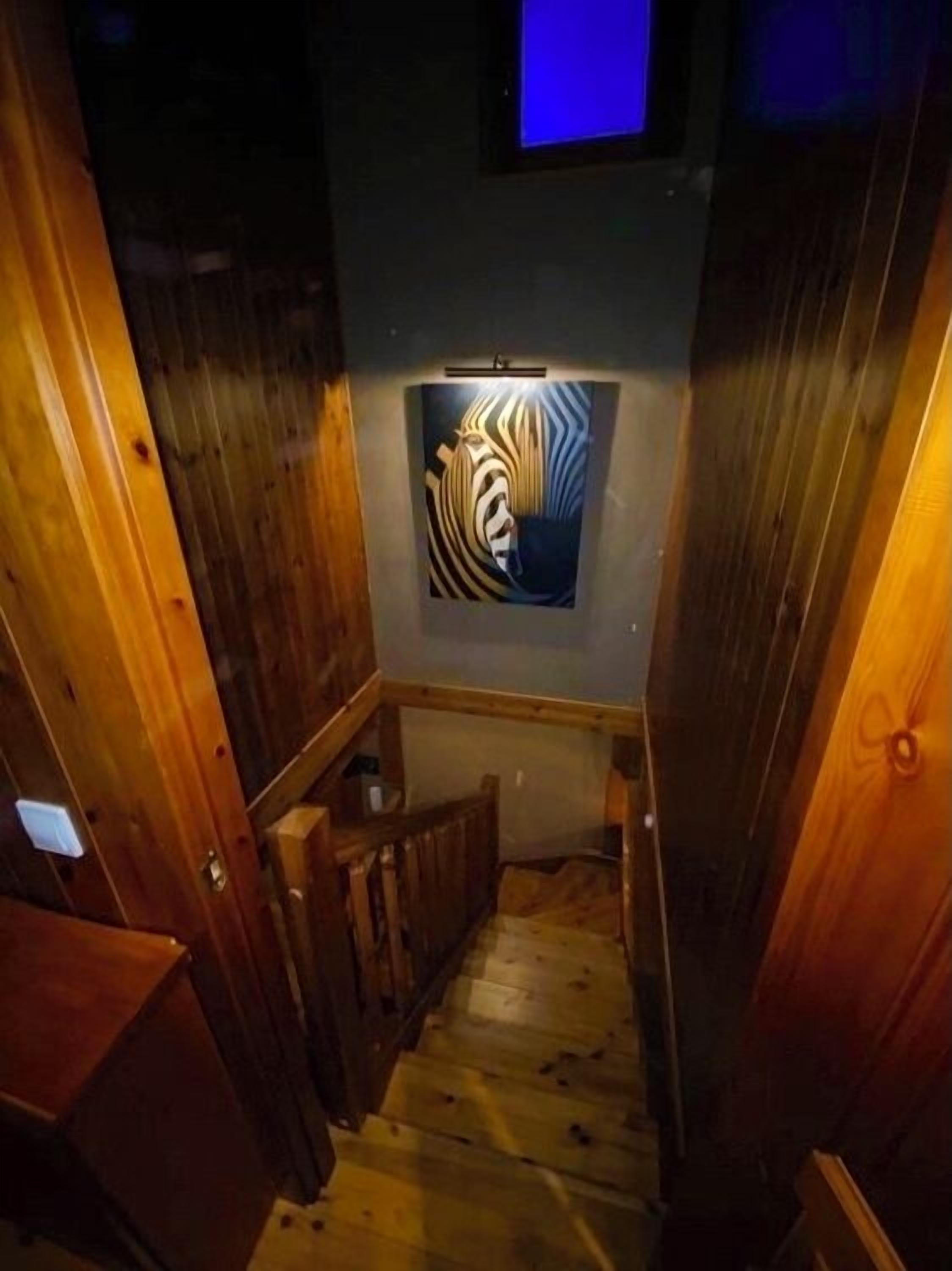 Una escalera de madera que lleva a una habitación con una obra de arte de pared a rayas de cebra.