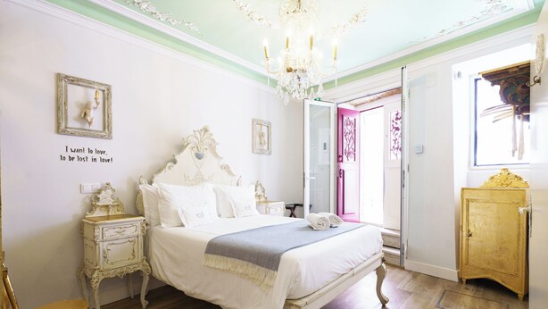 A bedroom with a large bed, a chandelier, a wooden cabinet, and a door with a pink design.