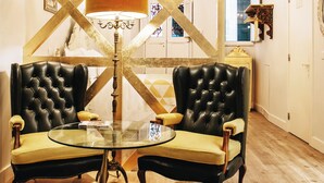 A room with a round glass table, two black leather chairs, a brass lamp, and a chandelier.