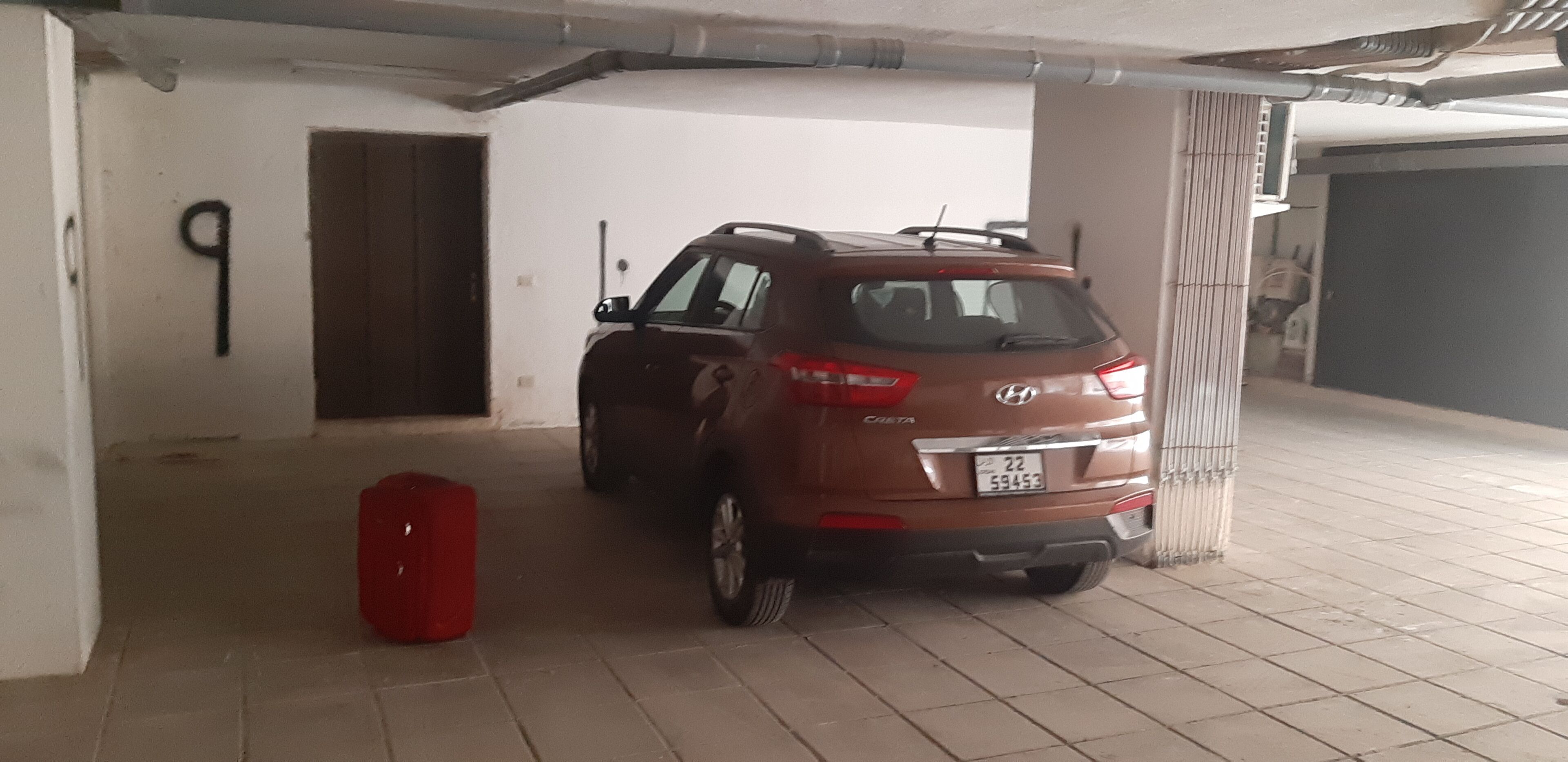 A parking garage with a brown SUV parked near a pillar, a red suitcase on the floor, and a door with the number 9.
