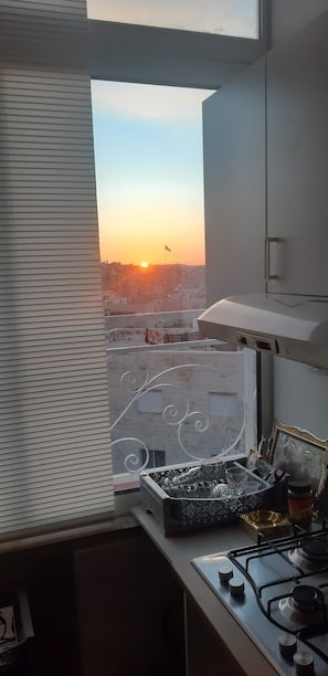 A kitchen with a window view of a sunset over a cityscape. - Marvelous Rooftop (Amman)