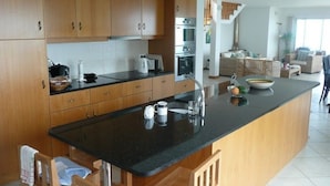 A modern kitchen with wooden cabinets, a black countertop, and a central island with a sink and kettle. - 3 bedroom villa and pool, Jardim do Mar, breathtaking view  (Jardim do Mar)