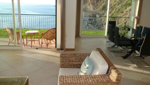 A living room with a wicker sofa, a TV, and a balcony with a view of the sea. - 3 bedroom villa and pool, Jardim do Mar, breathtaking view  (Jardim do Mar)