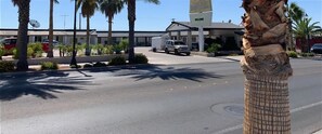A hotel entrance with palm trees, a parking lot, and a building with a sign. - The Sands Motel (Boulder City)
