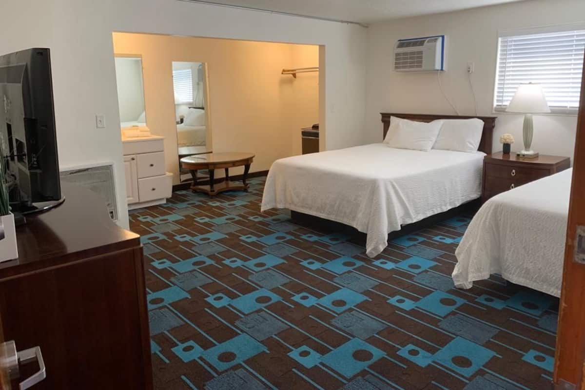 A hotel room with two beds, a desk, a television, and a bathroom visible through an open door.
