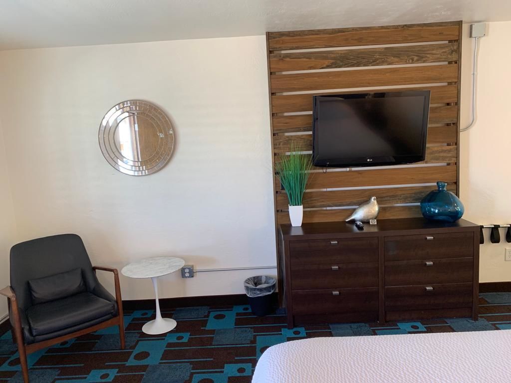 Habitació d'hotel amb un llit, un televisor fixat a una paret de panells de fusta, una taula rodona petita, una cadira, un taulell i un mirall decoratiu.