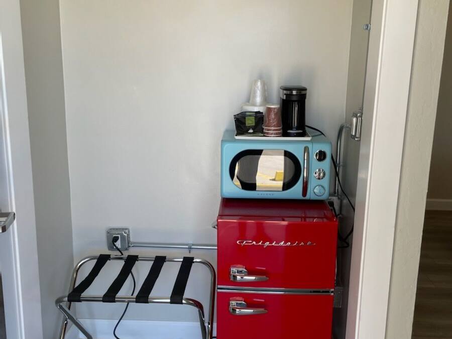 A compact kitchenette with a microwave, a red refrigerator, and a hanging clothes rack.