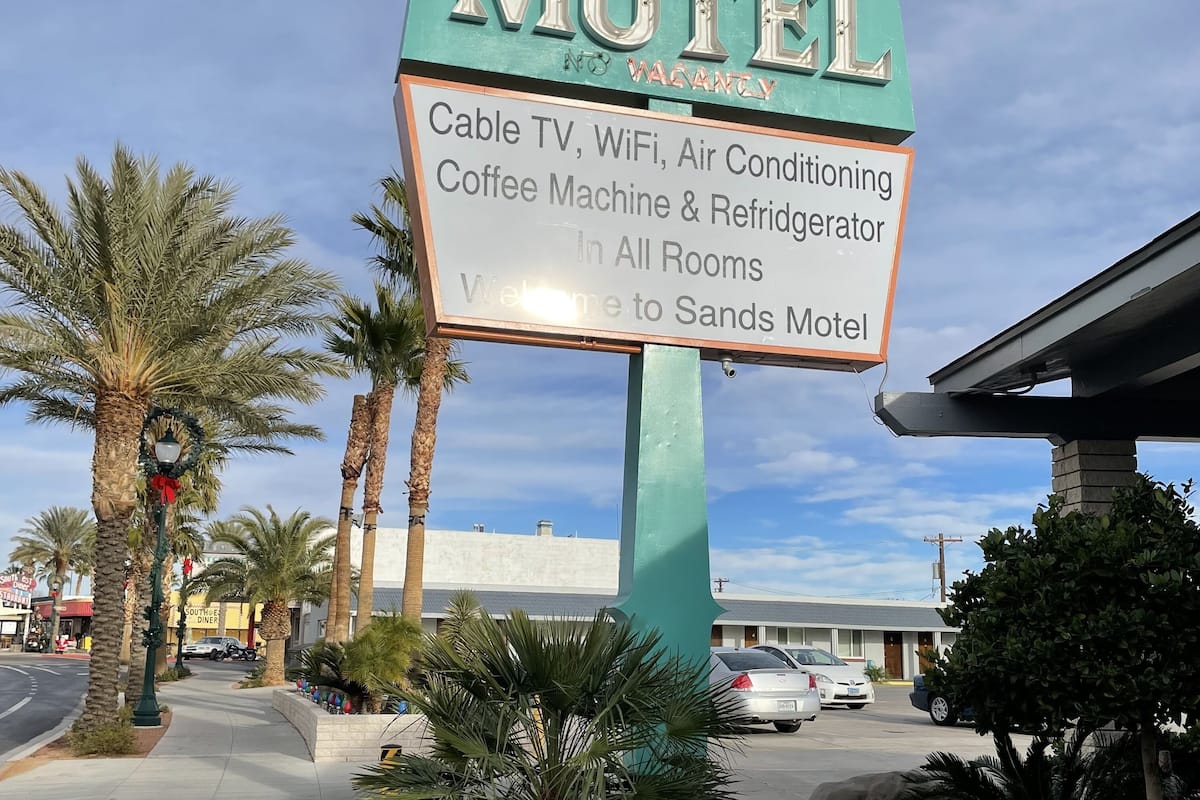 A sign for Sands Motel advertising amenities like cable TV, WiFi, air conditioning, coffee machine, and refrigerator in all rooms.