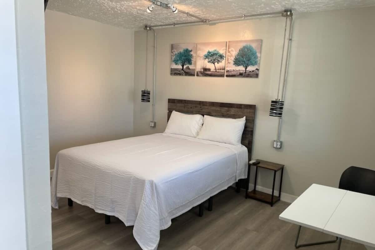 A bedroom with a bed, a small table, a chair, and a painting on the wall.