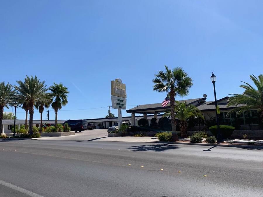 A hotel with a clear sky, palm trees, and a signboard.