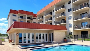 A multi-story building with a swimming pool, outdoor seating, and balconies. - 111 - Poolside 1 bedroom closest to the water (New Smyrna Beach)
