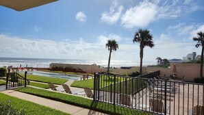 A pool area with a view of the ocean, palm trees, and a fenced patio with chairs. - 111 - Poolside 1 bedroom closest to the water (New Smyrna Beach)