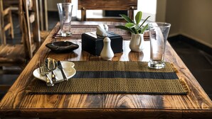 A wooden dining table set with cutlery, plates, a salt shaker, a pepper shaker, a glass, and a small potted plant. - Infinity Dhiffushi (Dhiffushi)