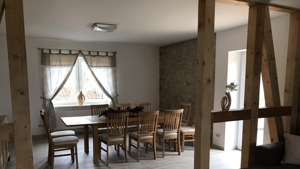 A dining area with a wooden table and chairs, a stone wall, and a window with curtains.