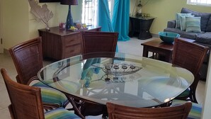 Un coin repas avec une table ronde en verre, entourée de chaises en osier dotées de coussins à rayures.