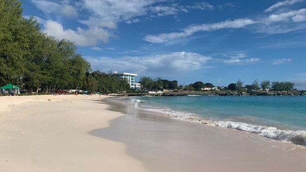 Une plage aux eaux cristallines, un rivage sablonneux et un bâtiment visible au loin.