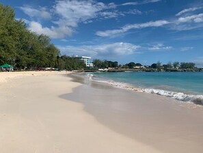 A beach with clear waters, a sandy shore, and a building in the background.