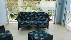 Un espace extérieur aménagé, abrité et doté d’un canapé bleu foncé et d’un pouf assorti, tous deux ornés d’un motif corail blanc.