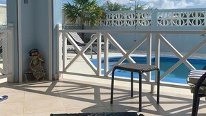 Un balcon avec une piscine, une balustrade blanche à claire-voie et une chaise.