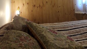 Une chambre avec des murs recouverts de panneaux de bois, un lit avec une literie à motifs floraux, un miroir et un appareil de climatisation.
