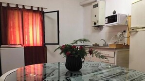 Une petite cuisine équipée d’un four à micro-ondes, d’un évier et d’un placard. On y trouve une table recouverte d’un set de table à motifs de journaux et une plante en pot.