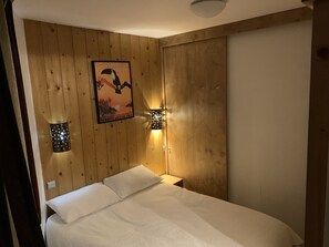 A bedroom with a wooden wall, a poster, a bed with white bedding, and two wall-mounted lights.