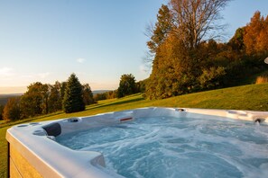 Un jacuzzi en un entorno natural, con una colina cubierta de hierba y árboles al fondo.